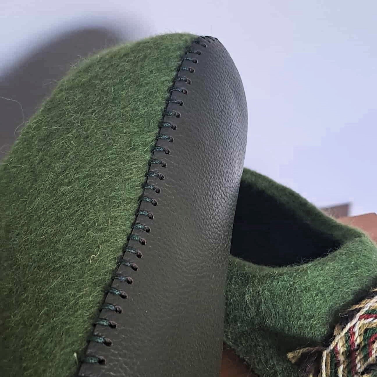 Detalus kadras: žali veltiniai su tautine juostele ir odinis padas su dekoratyvine siūle